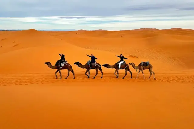 Viajeros montados en dromedarios avanzando por las dunas de Erg Chebbi, en Merzouga, al caer la tarde
